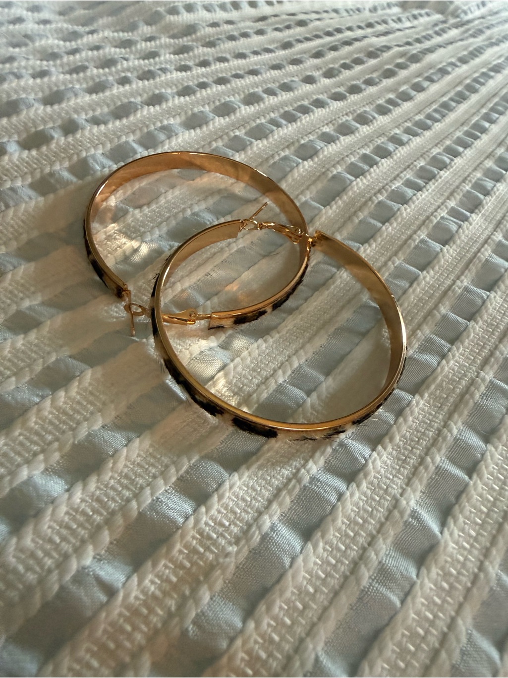 A pair of thin gold hoop earrings on a woven surface
